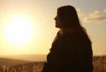 Uma pessoa refletindo ao pôr do sol, escrevendo em um diário de gratidão sobre momentos felizes do dia