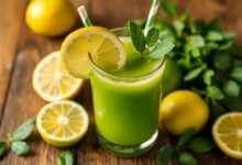 Copo de suco detox verde com ingredientes frescos como couve, limão e gengibre ao redor