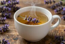 Xícara fumegante de chá de lavanda cercada por flores frescas em uma mesa de madeira rústica