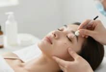 Pessoa aplicando cuidados suaves na pele para tratar espinhas, com um ambiente branco e produtos dermatológicos delicados