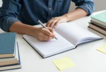 Pessoa estudando com cadernos, livros e post-its coloridos em uma mesa organizada, transmitindo concentração e entusiasmo