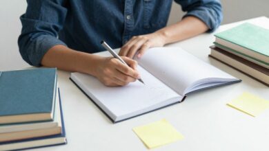 Pessoa estudando com cadernos, livros e post-its coloridos em uma mesa organizada, transmitindo concentração e entusiasmo