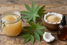 Uma variedade de adoçantes naturais como mel em um pote, folhas de stevia, açúcar de coco em uma tigela e xarope de bordo dispostos em uma mesa de madeira rústica com luz natural.