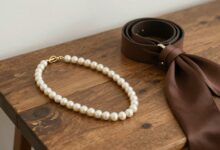 Uma coleção elegante de acessórios versáteis, como um colar de pérolas, um cinto de couro e um lenço de seda, artisticamente dispostos sobre uma superfície de madeira rústica.