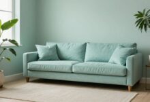 Uma sala de estar serena e minimalista, com paredes em um tom suave de verde sálvia, um sofá de linho bege, almofadas azuis e uma grande planta em um vaso de cerâmica, com luz natural suave entrando pela janela.