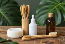 Uma composição elegante de vários produtos ecofriendly de uso diário, como uma escova de dentes de bambu, sabonete em barra, e um frasco de vidro, dispostos sobre uma superfície de madeira rústica com folhas verdes.