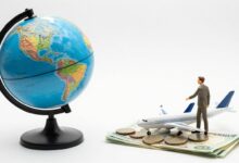 Um globo terrestre em miniatura sobre um monte de moedas e notas de dinheiro, com um avião de brinquedo ao lado, simbolizando viagens econômicas pelo mundo.