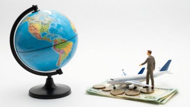 Um globo terrestre em miniatura sobre um monte de moedas e notas de dinheiro, com um avião de brinquedo ao lado, simbolizando viagens econômicas pelo mundo.