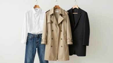 Um guarda-roupa cápsula elegantemente organizado com peças clássicas como um trench coat bege, uma camisa branca, jeans de corte reto e um blazer preto, em um ambiente minimalista e iluminado.