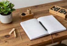 Uma mesa de madeira rústica com vários itens de hobbies analógicos, como um novelo de lã com agulhas, um diário aberto com uma caneta-tinteiro, uma planta em um vaso de cerâmica e peças de um jogo de tabuleiro.