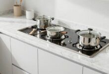 Uma cozinha moderna e impecavelmente limpa, com bancadas de mármore brilhando, armários brancos e utensílios de aço inoxidável organizados, banhada por uma luz natural suave.