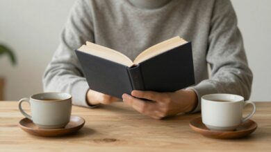 Uma pessoa sentada calmamente em um ambiente minimalista e iluminado, lendo um livro com uma xícara de chá ao lado, transmitindo paz e tranquilidade.