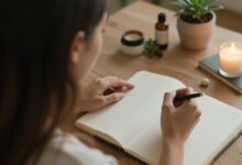 Pessoa sentada em um ambiente tranquilo praticando autocuidado emocional, com luz natural, diário e elementos de bem-estar ao redor