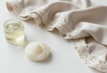 Roupas delicadas de seda, renda e lã organizadas sobre uma superfície clara, com sabão suave e elementos de lavanderia cuidadosa ao redor