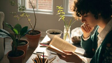 Pessoa aproveitando um momento tranquilo em casa, lendo, desenhando e cuidando de plantas, com materiais de hobbies organizados em uma mesa iluminada pela janela.
